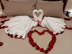 A bed with white towels arranged in a heart shape and a heart-shaped towel arrangement on the pillows. - Hotel Danini (Teziutlan)