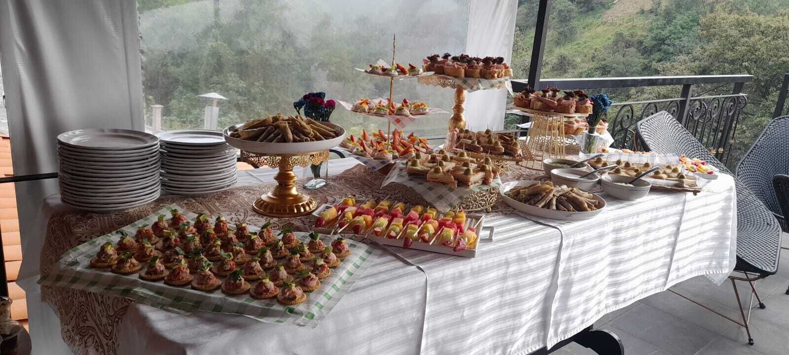 A buffet table with various food items and plates, set against a scenic outdoor backdrop.
