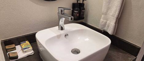 Un baño con un lavabo blanco, un espejo, un perchero para toallas y artículos de aseo.