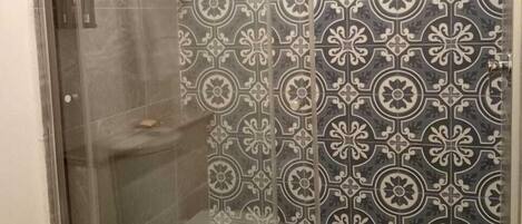 Ducha con mampara de vidrio con diseño, inodoro y lavamanos.