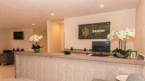 A reception area with a reception desk, a mounted logo, a television, and potted plants. - Hotel Danini (Teziutlan)
