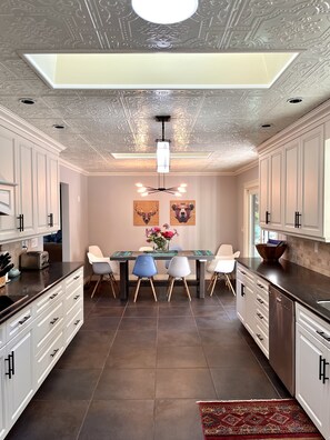 A modern kitchen with white cabinetry, a central island with chairs, a ceiling light fixture, and a decorative ceiling. - Magical Farm Villa with Heated Salt Water Pool (Duncan)