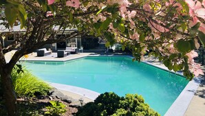 Una piscina rodeada de abundante vegetación y flores rosadas.