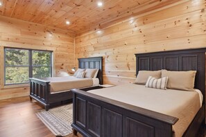 Cozy cabin-style bedroom with two beds, a large window, and a patterned rug.