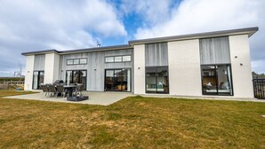 Une maison moderne à deux étages dotée d’un patio comprenant un barbecue et un espace salon extérieur.