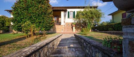 A stone pathway leading to a building with a tiled roof and a small staircase.