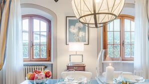 A dining area with a table set for two, a chandelier, and a view of the garden through the windows. - Villa Cesare Convenient and Smart (Lucca)