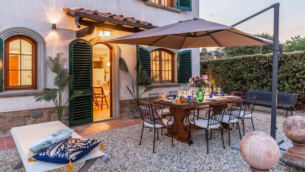 A patio with a table set for dining, surrounded by chairs, and a large umbrella providing shade. - Villa Cesare Convenient and Smart (Lucca)