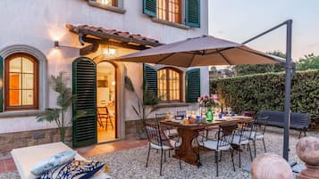 Un patio con una mesa lista para comer, rodeada de sillas y una gran sombrilla que da sombra.