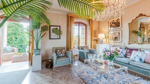 A spacious living room with a large chandelier, comfortable seating, and a view of greenery outside. - Villa Cesare Convenient and Smart (Lucca)