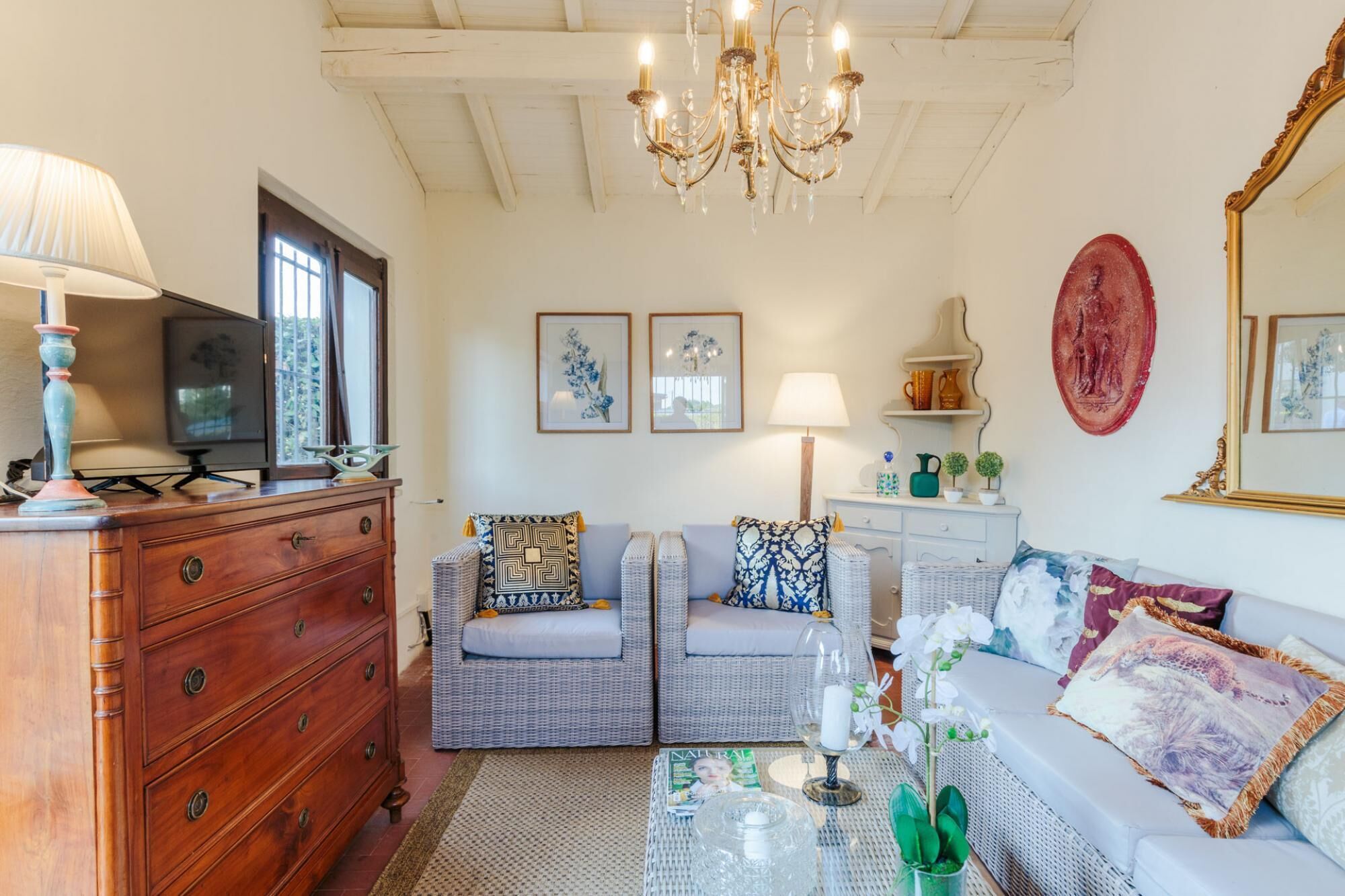 A cozy living room with wicker furniture, a wooden dresser, and a chandelier.