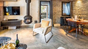 Una sala de estar moderna con una pared de piedra, una chimenea, una mesa de comedor con sillas y un televisor montado en la pared.