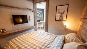 Un dormitorio con colcha a cuadros, televisor montado, cuadro de cabeza de venado enmarcado y ventana con vista a un paisaje nevado.
