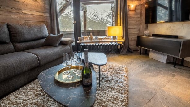 Una sala de estar moderna con un sofá, una mesa de centro con copas de vino y una botella, un televisor y una chimenea.