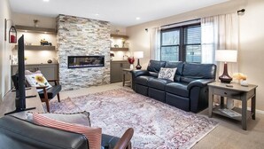 Ein Wohnzimmer mit Kamin aus Stein, einer Ledersofa, einem Couchtisch und einem Fernseher.