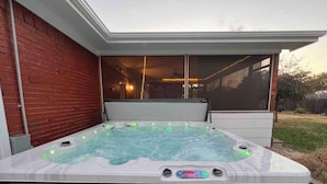 Ein Whirlpool mit Bedienfeld, eine Ziegelwand und eine Glastür zu einer überdachten Terrasse.