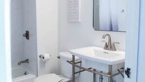 A small bathroom with a white sink, a toilet, and a shower. There is a mirror above the sink and a sign on the wall. - Downtown close to UAB, St. Vincent’s, BJCC and Airport  (Birmingham)