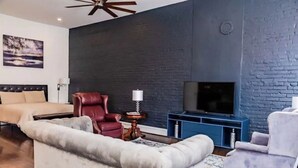 A modern living room with a large grey sofa, a red armchair, a beige sofa, a television on a blue stand, and a ceiling fan. - Downtown close to UAB, St. Vincent’s, BJCC and Airport  (Birmingham)