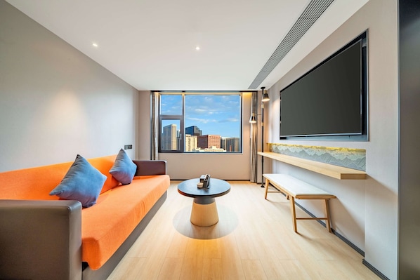 A modern living room with a large window, a sofa, a coffee table, and a flat-screen TV mounted on the wall. - Hilton Garden Inn Chengdu Kuanzhai Alley (Chengdu)