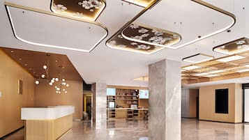 A modern reception area with a wooden reception desk, a large pillar, and a ceiling with geometric light fixtures.
