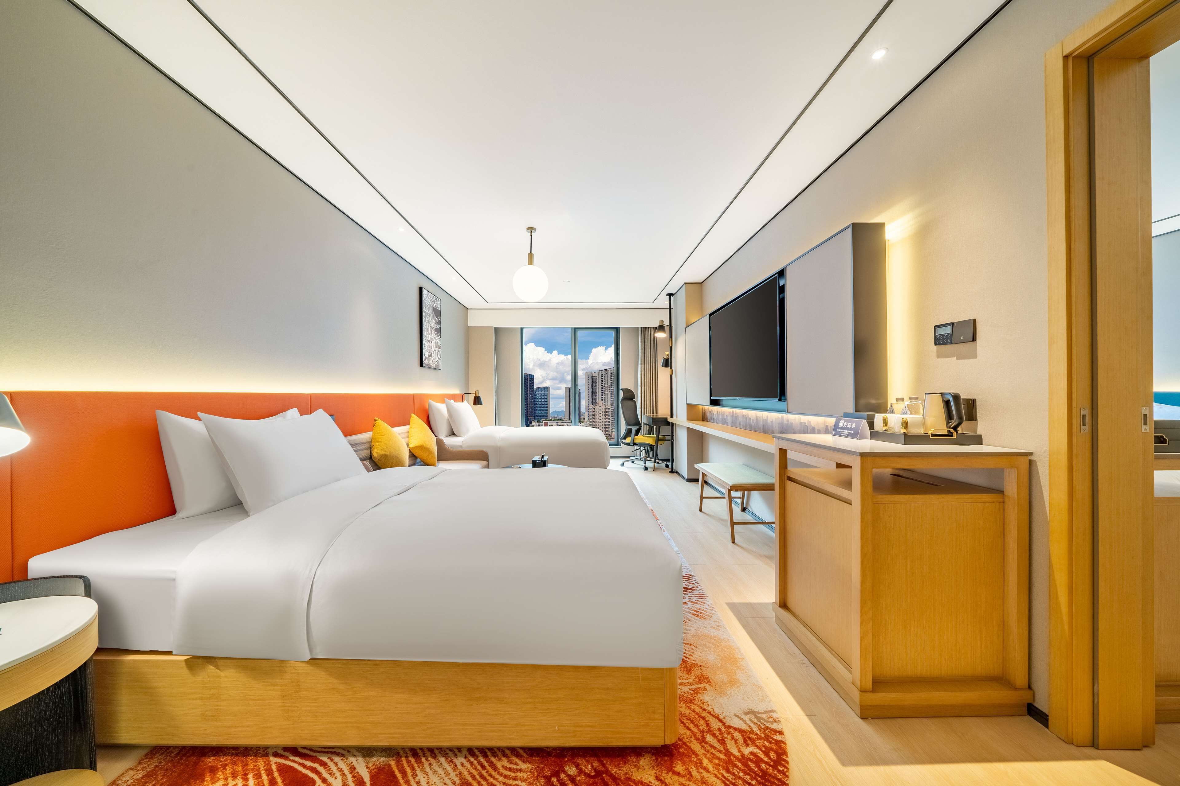 A modern hotel room with a large bed, a desk, a TV, and a city view.