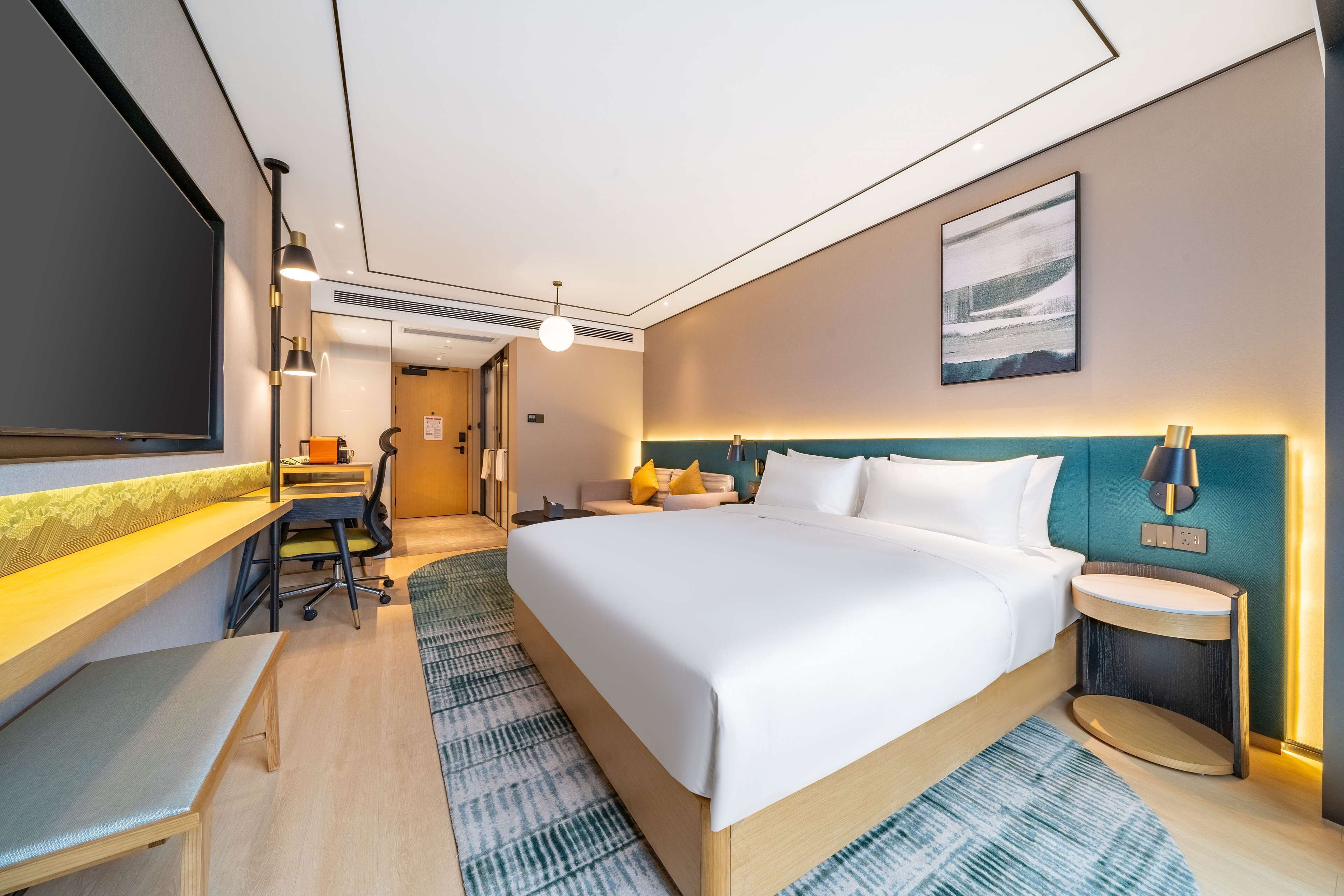 A modern hotel room with a large bed, a desk, and a seating area.