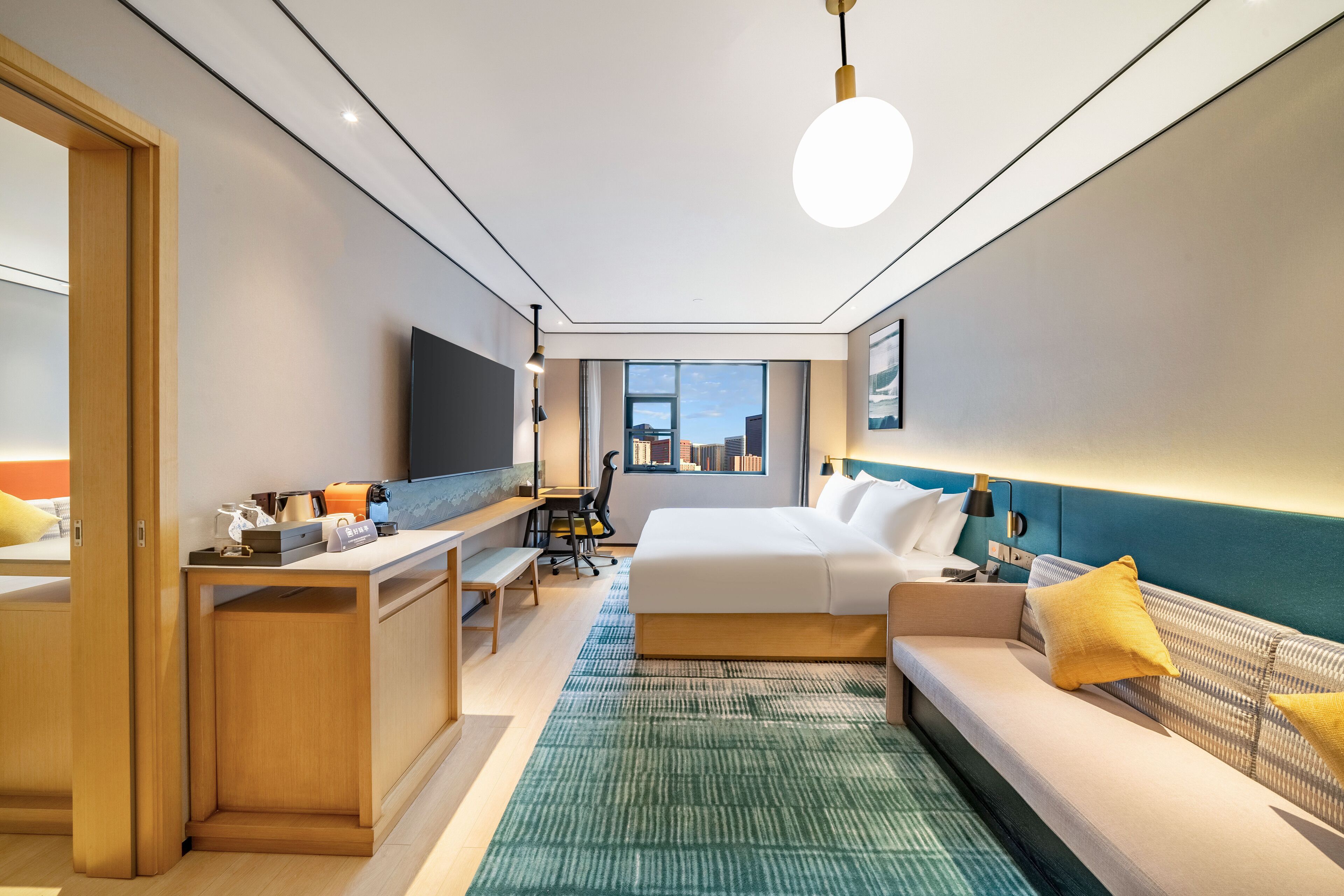 A modern hotel room with a bed, a sofa, a desk, and a television.