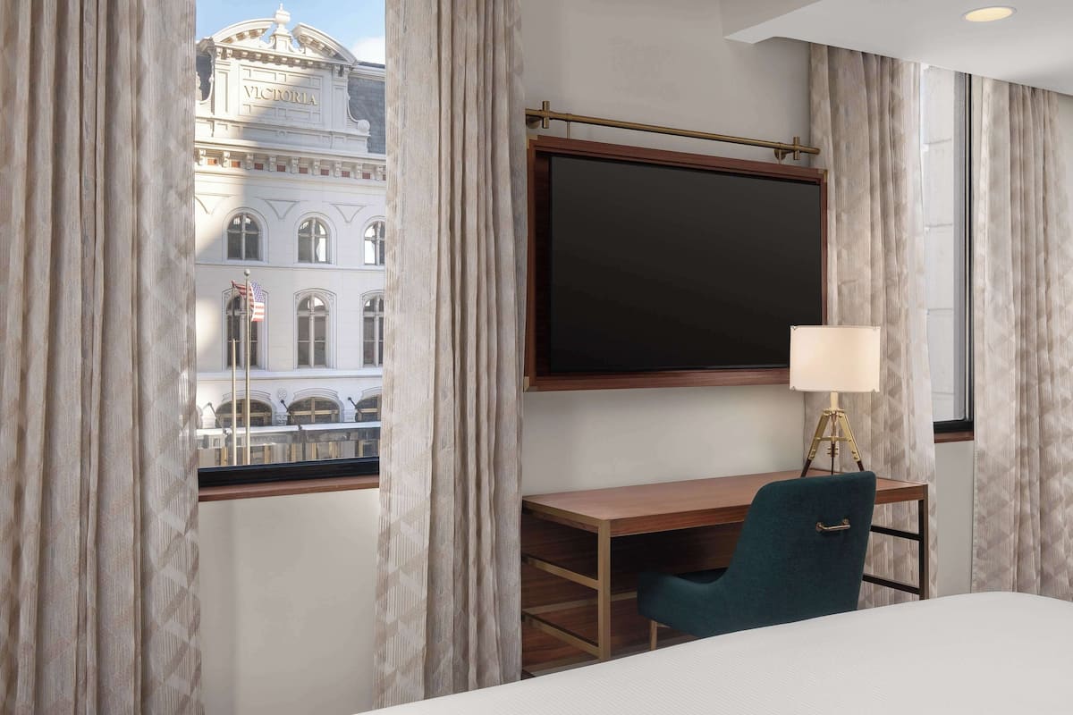 Ett hotellrum med ett stort fönster, ett skrivbord, en stol och en säng.