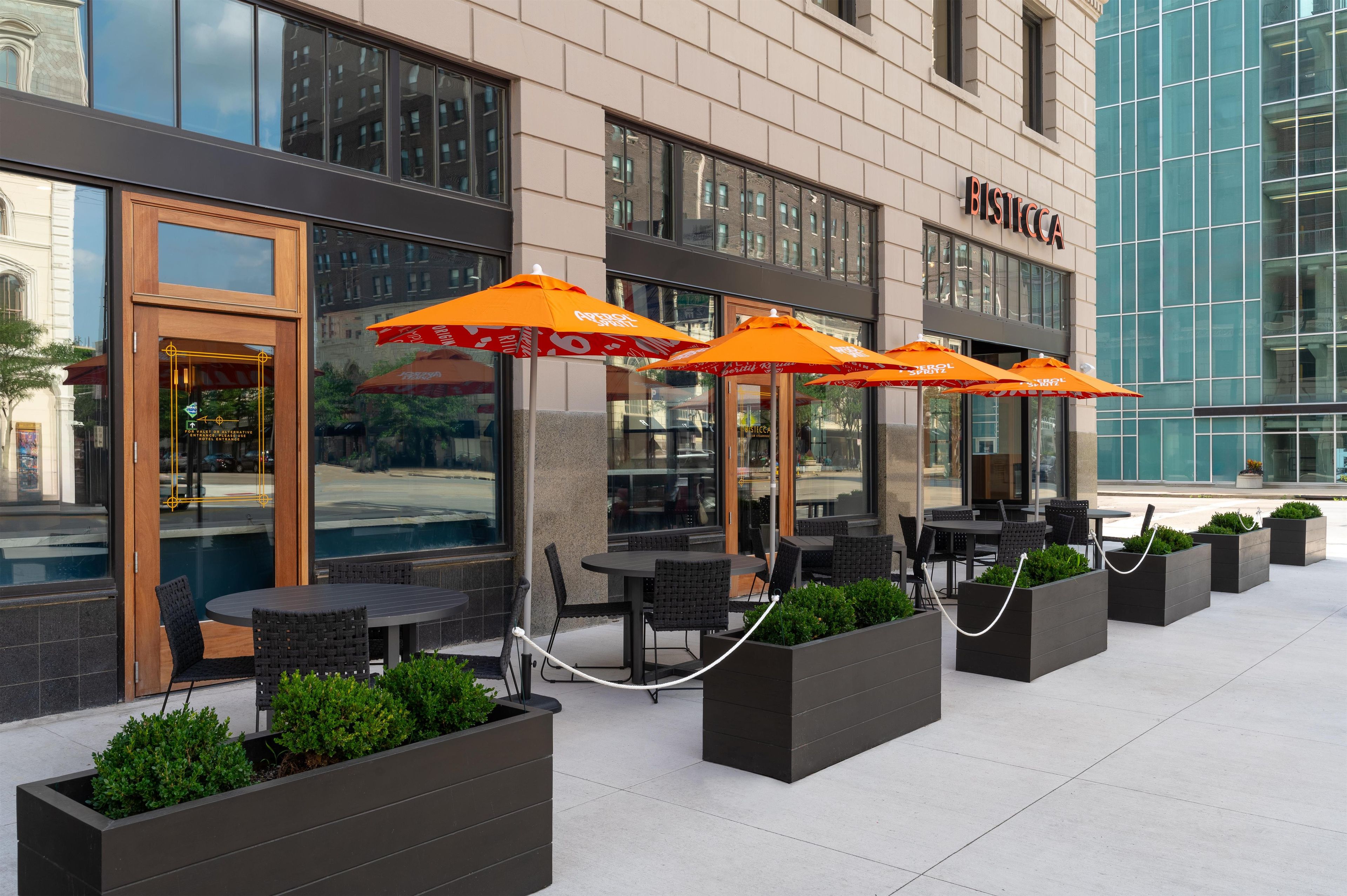 A hotel exterior with outdoor seating, large windows, and a clear view of the street.