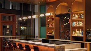 Una zona de bar con una barra larga, taburetes rojos y estantes llenos de botellas.