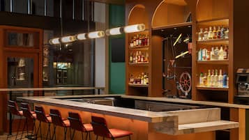 A bar area with a long counter, red bar stools, and shelves stocked with bottles.