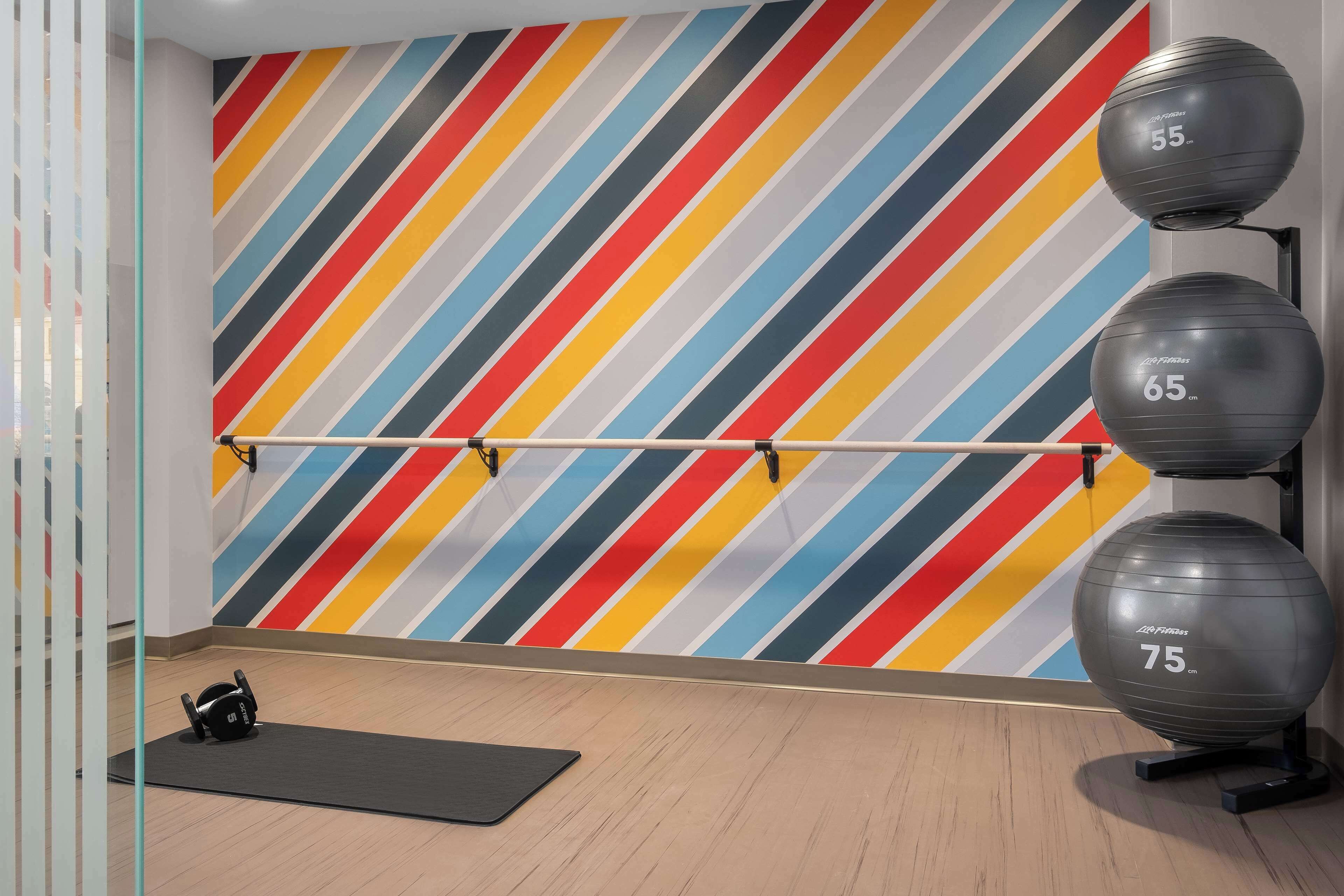 Ett gym med en vägg som har färgglada ränder, träningsbollar och ett ställ för skivstänger.