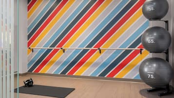 Ett gym med en vägg som har färgglada ränder, träningsbollar och ett ställ för skivstänger.