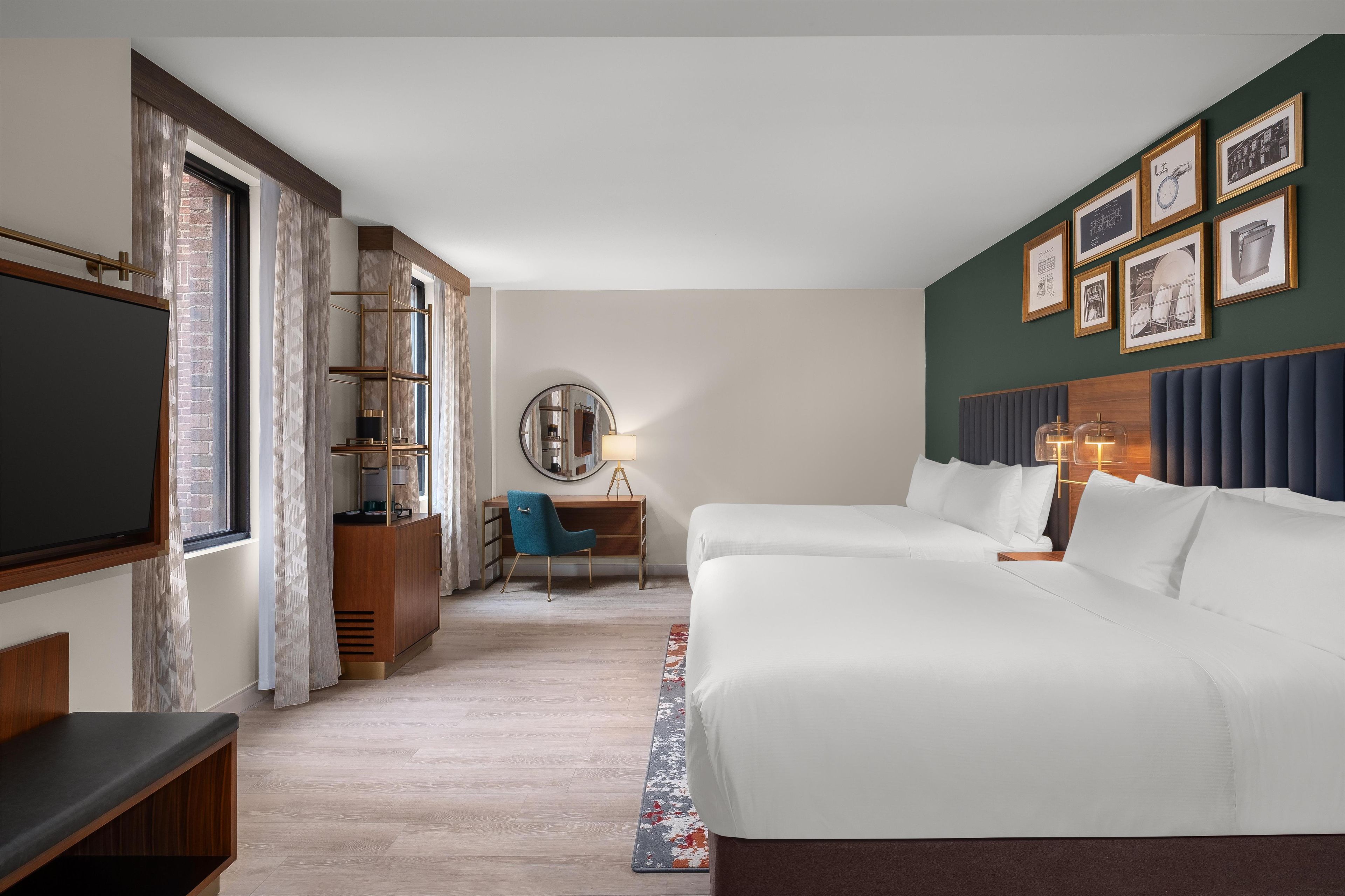 A hotel room with a large bed, a desk, a chair, a television, and a wall with framed pictures.