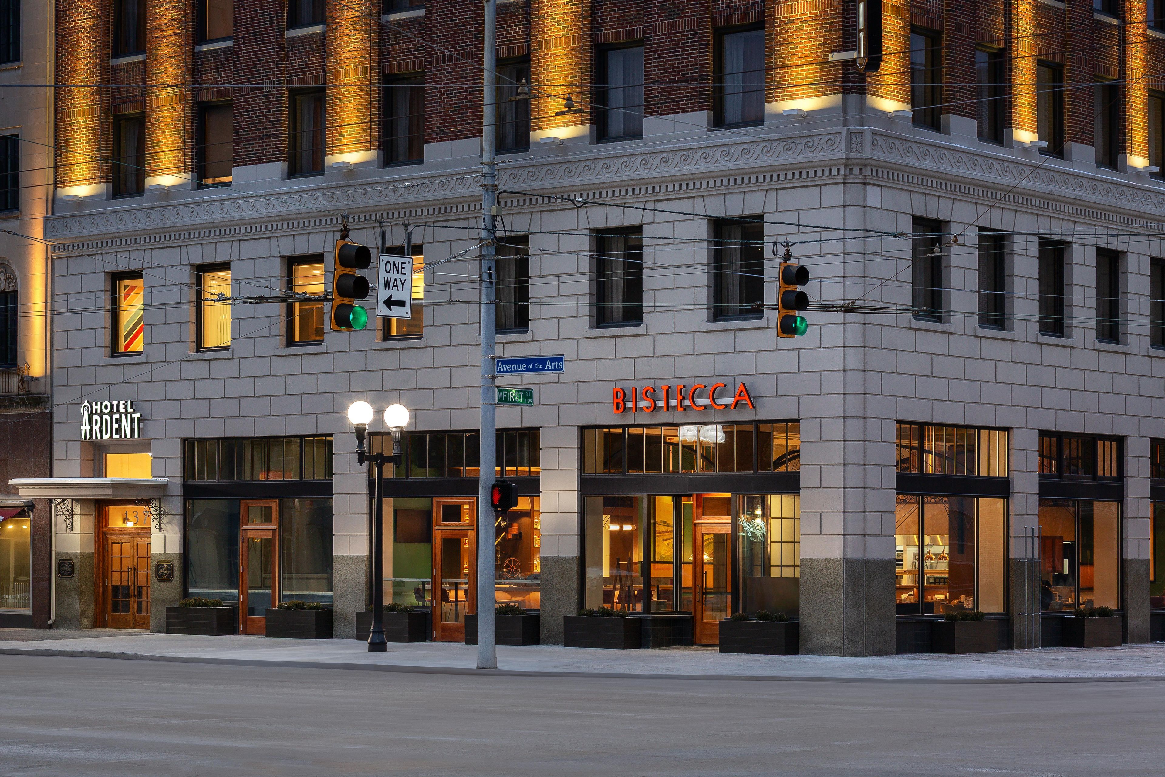 A corner building with a 'Hotel Ardent' sign, 'Bistecca' restaurant, and a 'One Way' street sign.