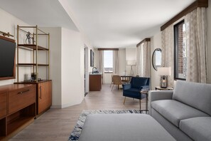 A modern hotel room with a flat-screen TV, wooden furniture, a dining area, and a view of the city. - Hotel Ardent Dayton Downtown, Tapestry Collection By Hilton (Dayton)