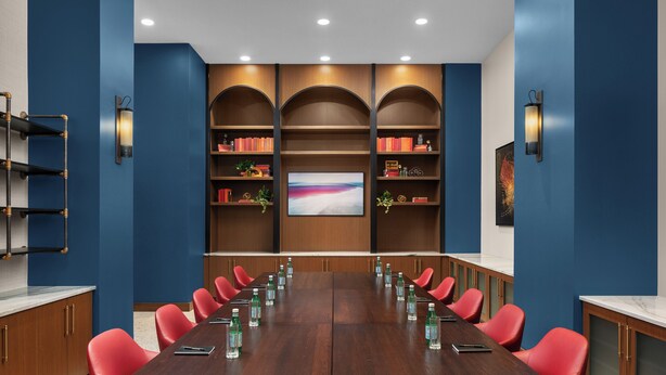 A conference room with a long table, red chairs, and bookshelves with books and decorative items.