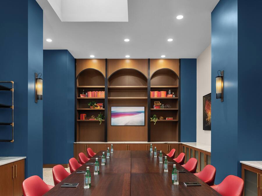 A conference room with a long table, red chairs, and bookshelves with books and decorative items.