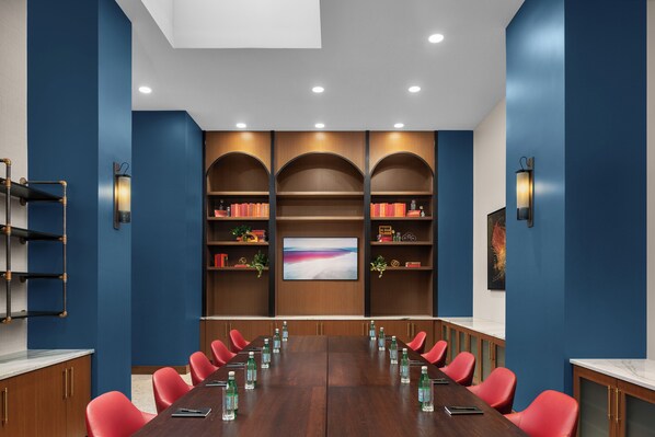 Un salón de conferencias con una larga mesa, sillas rojas y estanterías con libros y adornos.