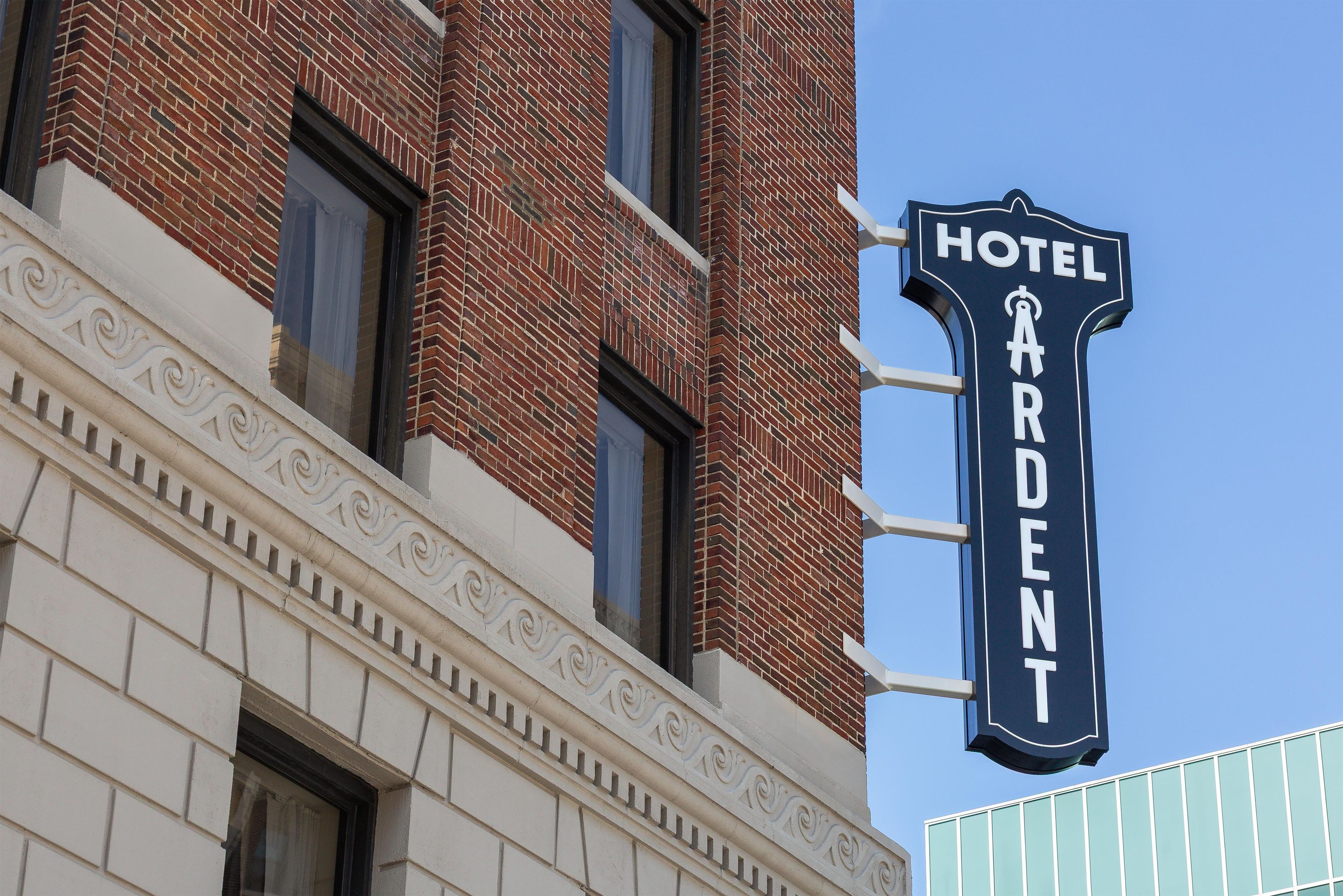 Een hotelschild met de naam 'Hotel Ardent' bevestigd aan een gebouw met een bakstenen gevel en klassieke architectuurdetails.