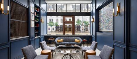 A modern lounge area with seating, bookshelves, and a view of the street.