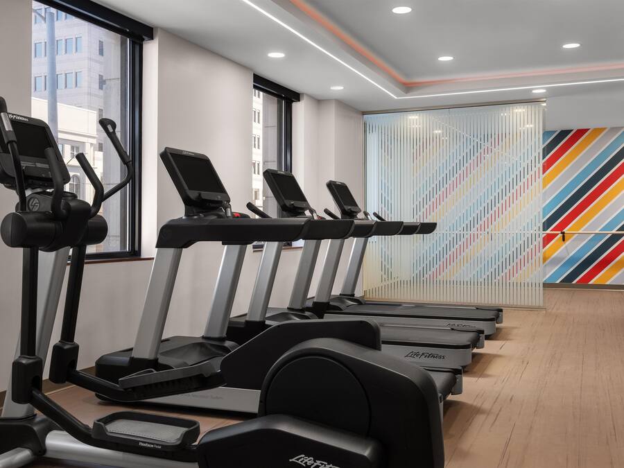 A row of treadmills in a gym with a colorful striped wall in the background.