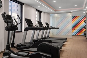 Varias cintas de correr en un gimnasio, con un muro multicolor a rayas de fondo.