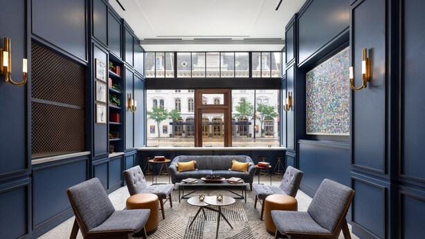 Un espacio lounge moderno con un conjunto de sofás, sillones y una mesa de centro, destacando un amplio ventanal con vistas a la ciudad.