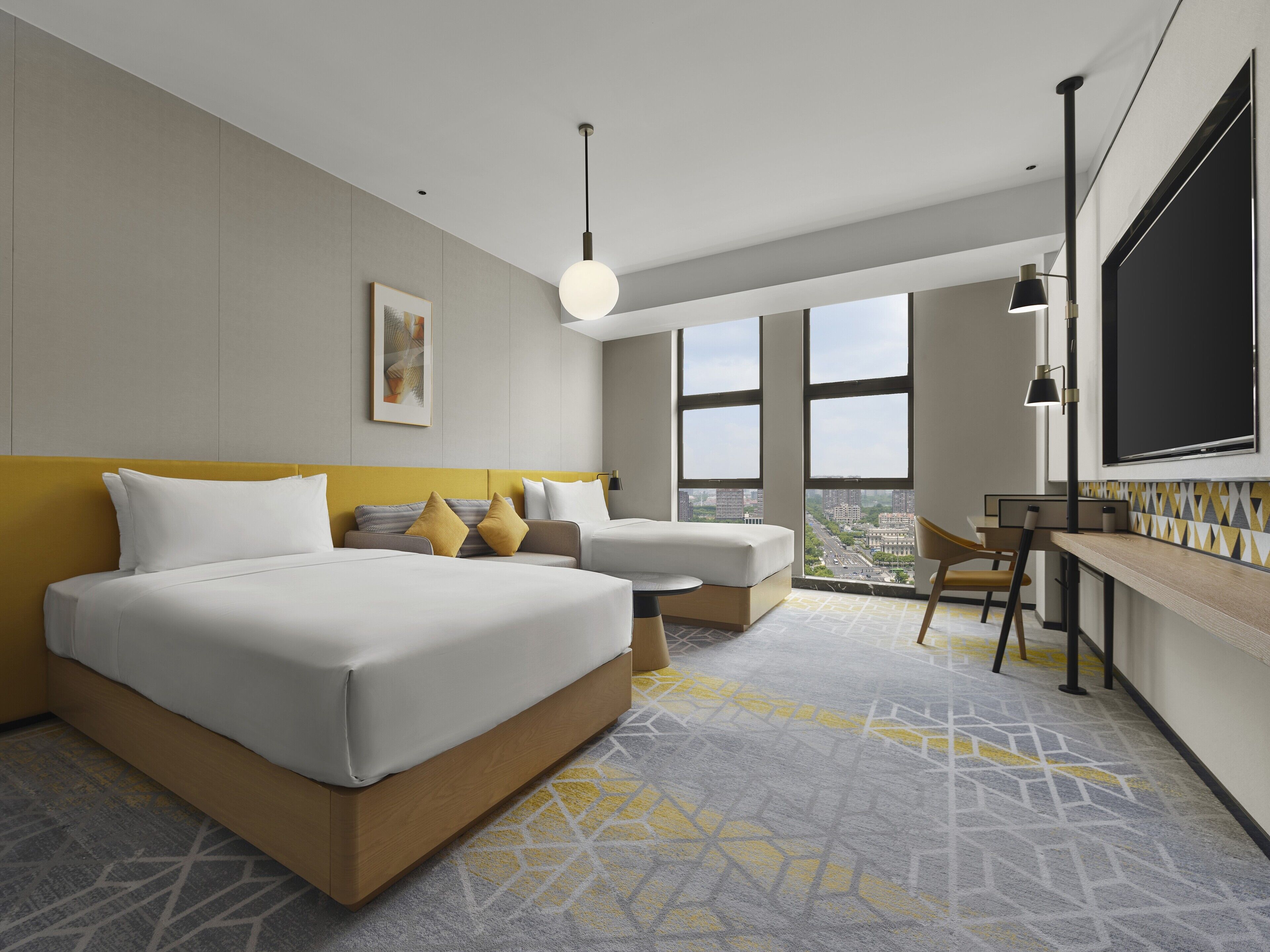 A modern hotel room with a large bed, a desk, and a view of the city through large windows.