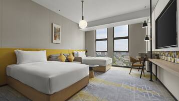 Quarto de hotel moderno com uma cama grande, uma escrivaninha e vista da cidade através de amplas janelas.