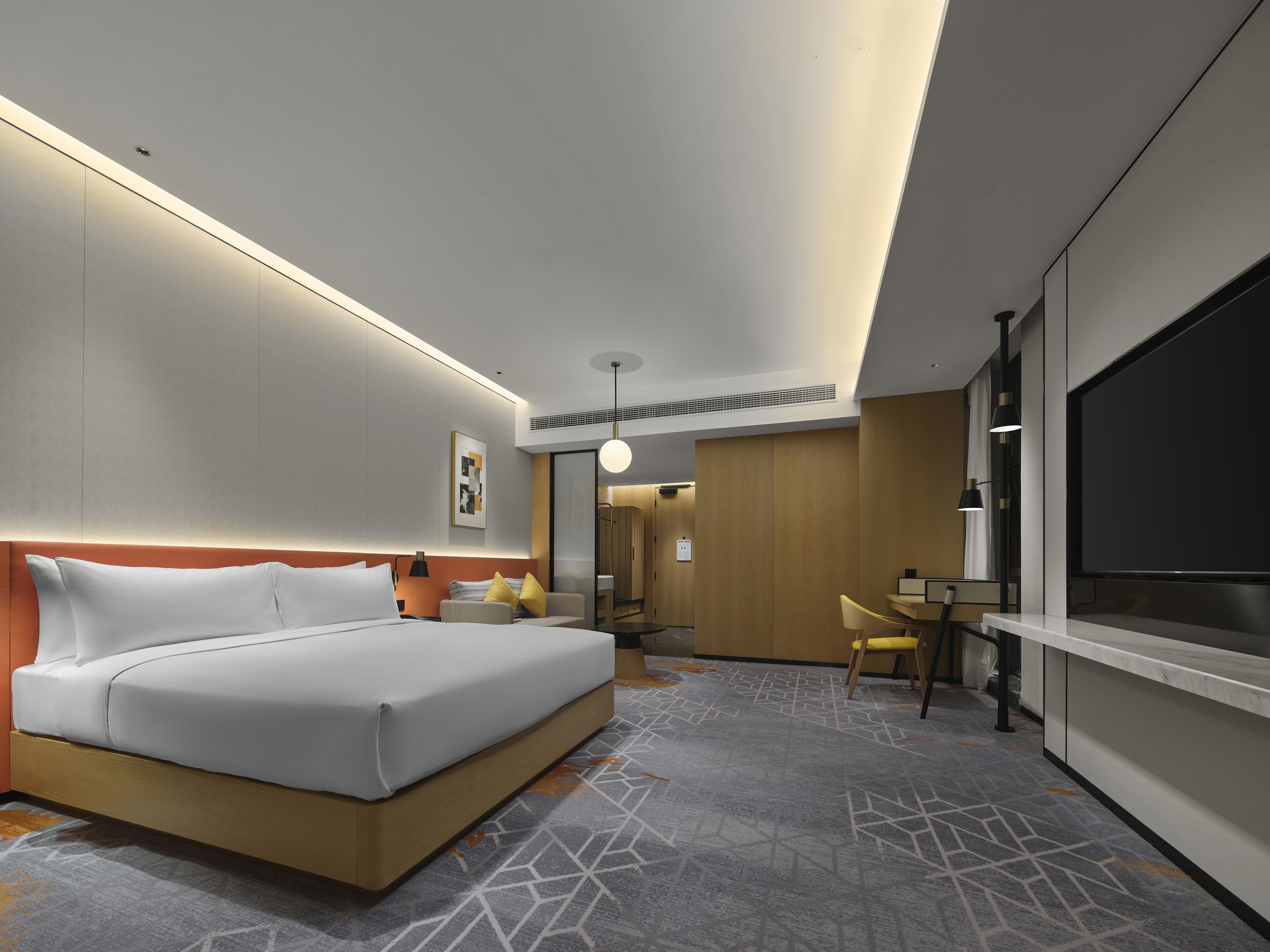 A modern hotel room with a large bed, a desk, a chair, and a TV.