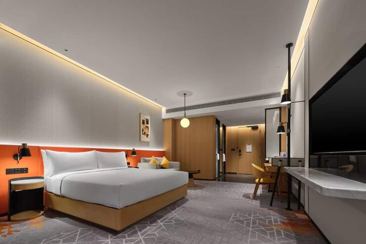 Ein modernes Hotelzimmer mit einem großen Bett, einem Schreibtisch, einem Fernseher und einer separaten Sitzecke.