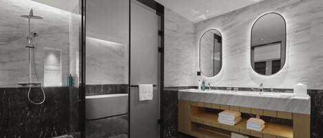 Un baño moderno con cabina de ducha de vidrio, tocador de mármol y dos espejos ovalados montados en la pared.