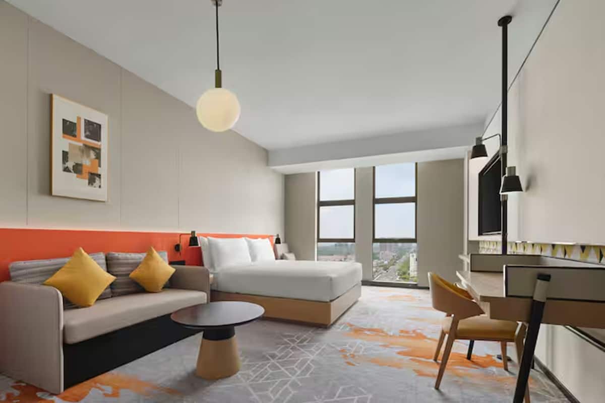 Ein modernes Hotelzimmer mit Sofa, Bett, Schreibtisch und Blick auf die Stadt.